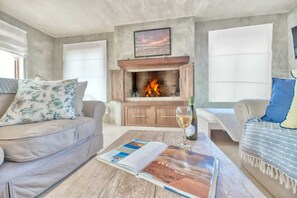 Ein Wohnzimmer mit Kamin, einer Couch, einem Couchtisch mit einer Zeitschrift und einer Weinflasche.
