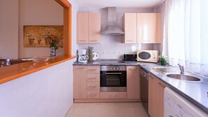 Eine kleine Küche mit Holzausstattung, einem Edelstahlbackofen, einer Mikrowelle und einem Spülbecken.