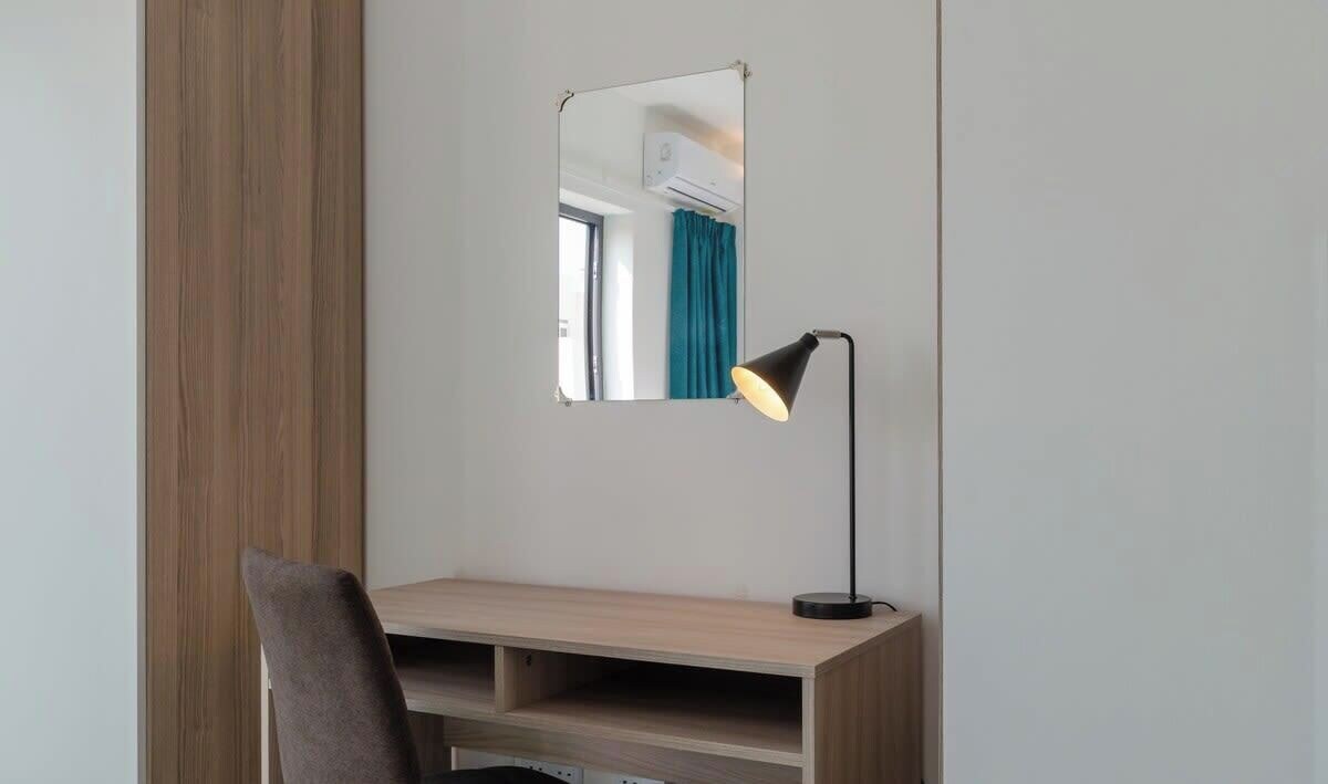 Un bureau avec un miroir, une lampe et une chaise, dans une pièce dont le mur est uni.