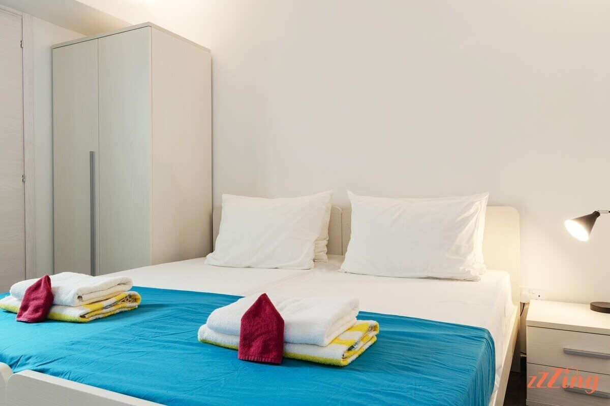 A hotel room with a bed, a wardrobe, and a nightstand with a lamp.