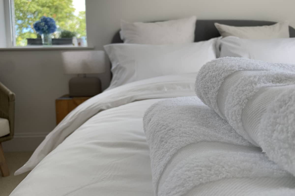 Cama bem arrumada com lençóis brancos e toalha branca dobrada.