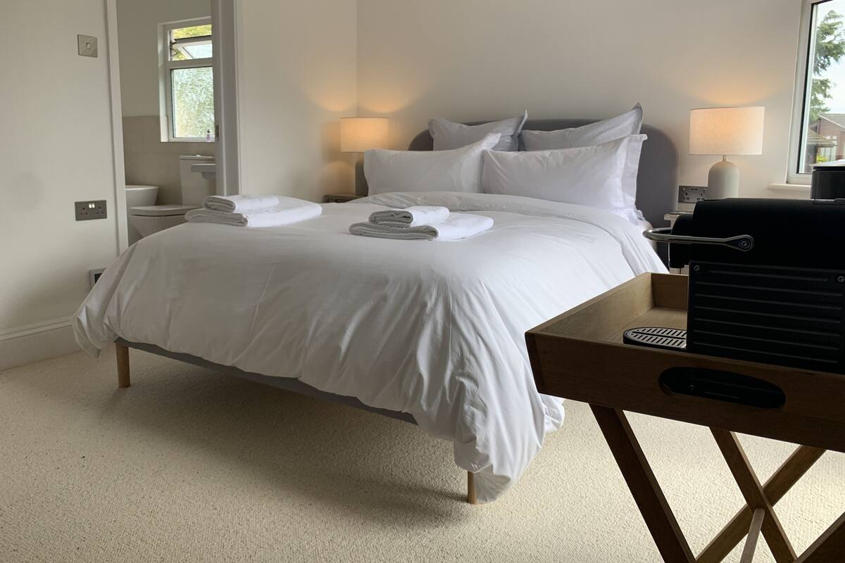 Quarto de hotel com cama, duas luminárias de cabeceira, uma escrivaninha de madeira com um controle remoto e um espelho na parede.