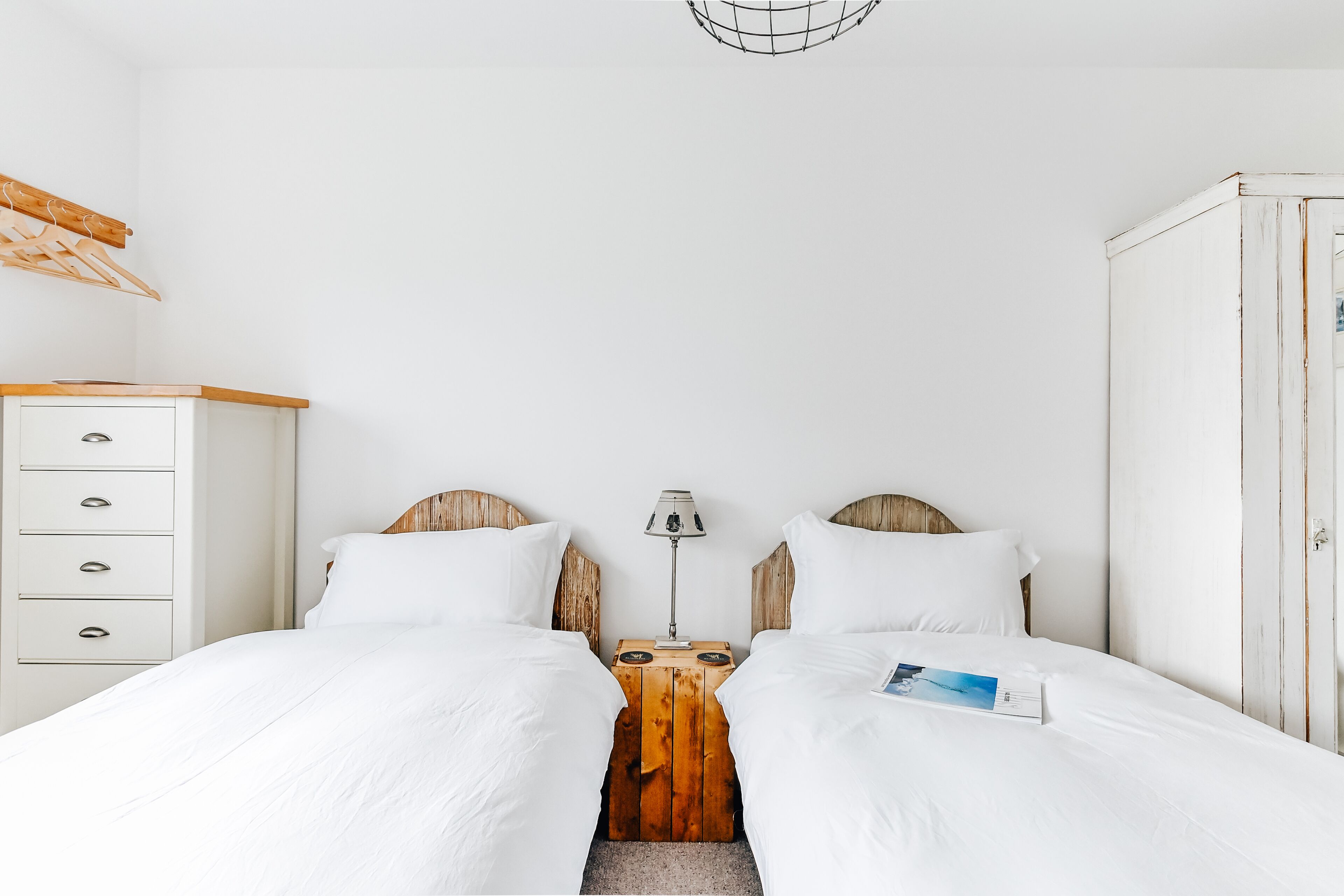 A double bed with white bedding, a wooden nightstand with a lamp, and a white wardrobe.