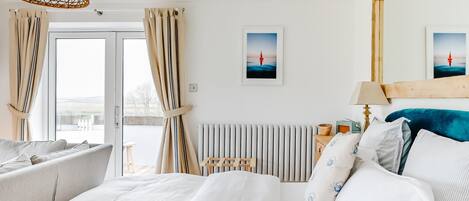 A hotel room with a bed, a wooden headboard, a radiator, a lamp, and a window with curtains.