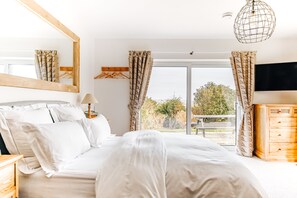 Un dormitorio con cama, cómoda de madera, televisor y balcón con cortinas.