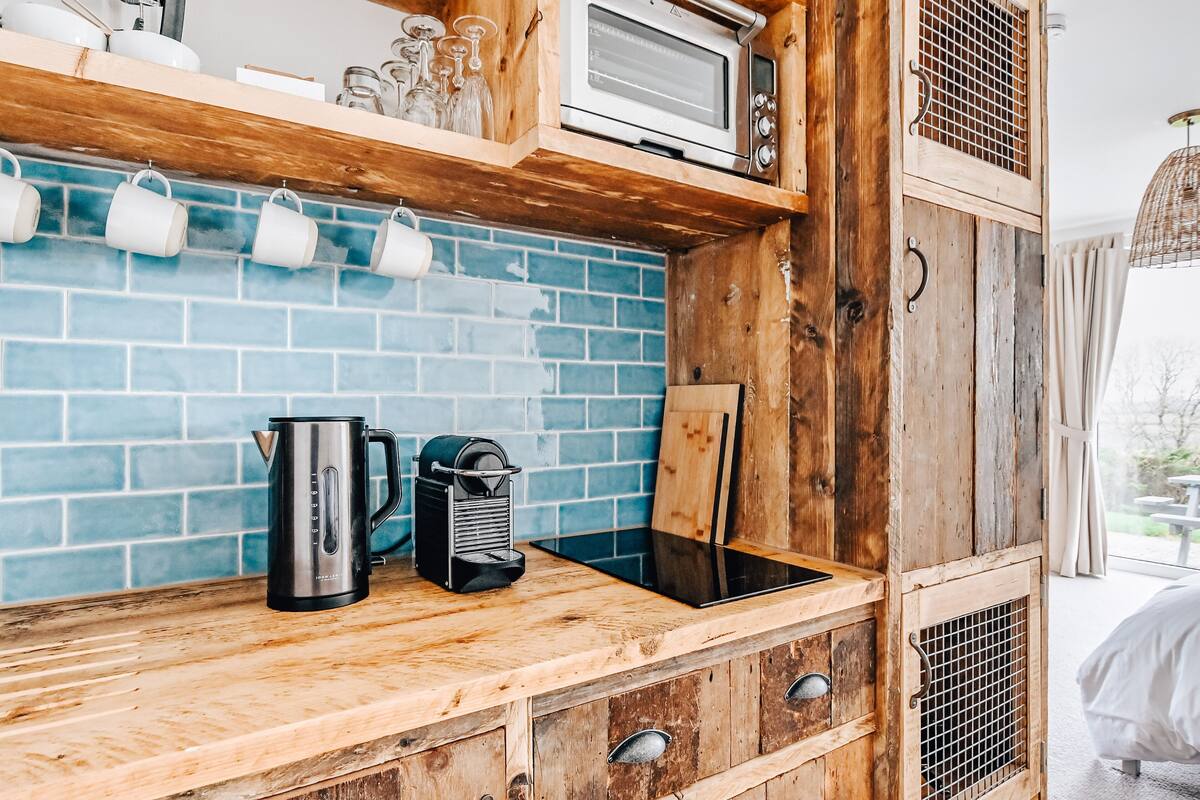 Uma cozinha compacta com micro-ondas, cafeteira e chaleira em bancada de madeira.