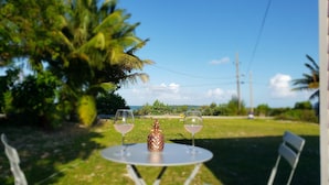 Una mesa con dos copas de vino y un adorno en un césped con vistas al océano y palmeras.