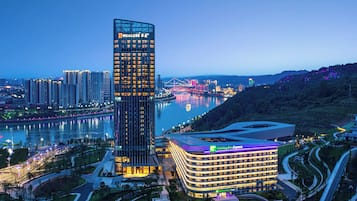 A modern hotel with a curved facade, located near a river with a bridge in the background.