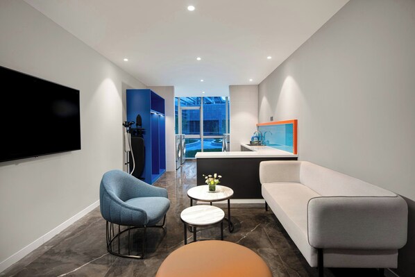 Un salon moderne avec un téléviseur, deux fauteuils, un canapé, une table basse et une vue sur un bâtiment à l’extérieur.