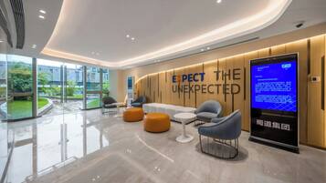 Een moderne lobby met een groot digitaal scherm, een zithoek en uitzicht op groen buiten.