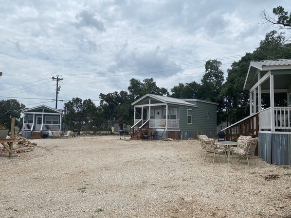 A row of small, single-story houses with porches, surrounded by gravel and trees.