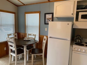 A compact kitchen with a dining table, chairs, a refrigerator, a stove, and a microwave.