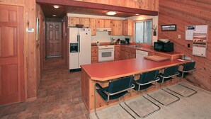 A wooden cabin-style kitchen with a central island, built-in appliances, and a dining area with bar stools. - Cozy 3 bed, 2 bath, Pet Friendly home. HOT TUB! (Black Butte Ranch)