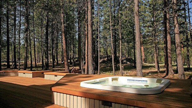 A hot tub in a forested area with wooden deck seating. - Cozy 3 bed, 2 bath, Pet Friendly home. HOT TUB! (Black Butte Ranch)