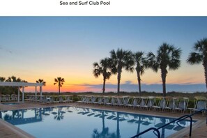 Une piscine avec des chaises longues et des palmiers, au coucher du soleil.
