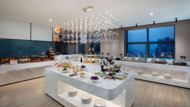 A modern hotel lobby with a marble reception desk, a chandelier, and a large window offering a city view. - Ramada by Wyndham Huangshi Huangshigang (Huangshi)