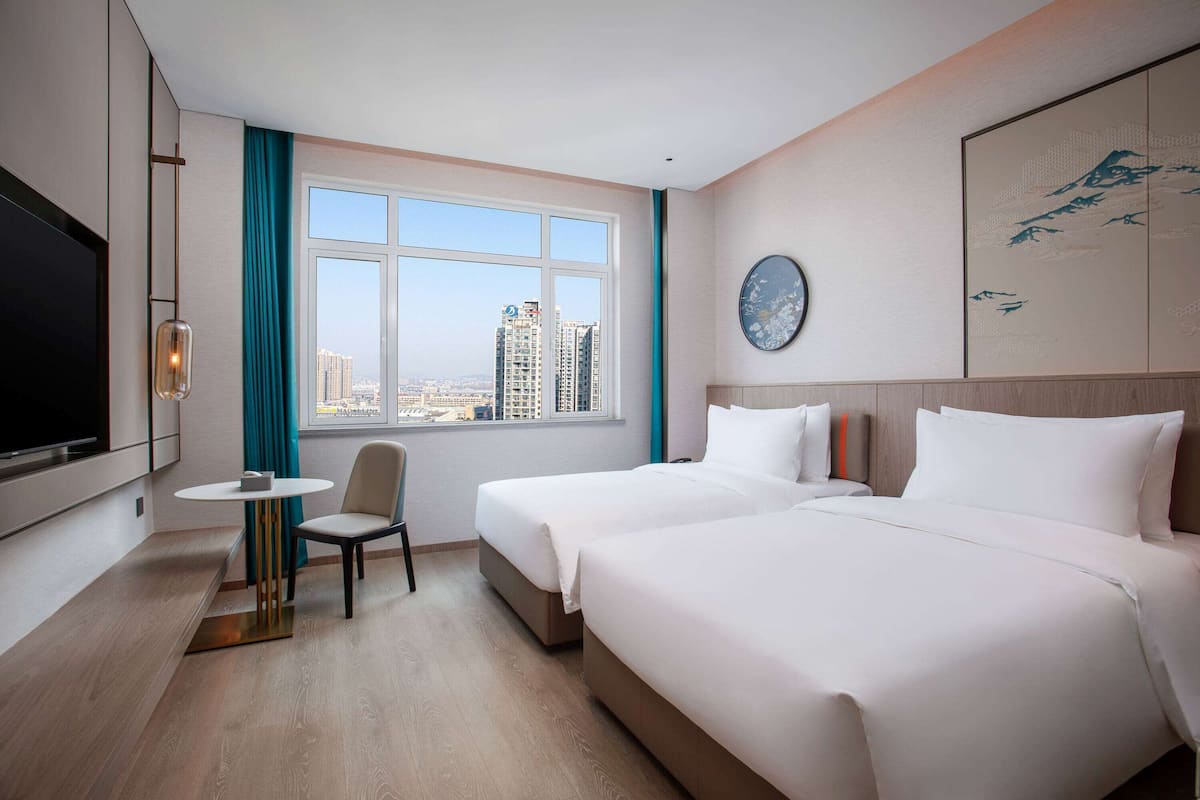 A hotel room with two beds, a TV, a small table, and a chair.
