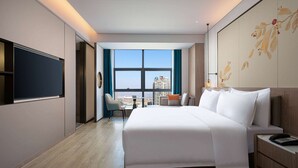 A modern hotel room with a large bed, a flat-screen TV, a desk with a chair, and a view of the city through a large window. - Ramada by Wyndham Huangshi Huangshigang (Huangshi)