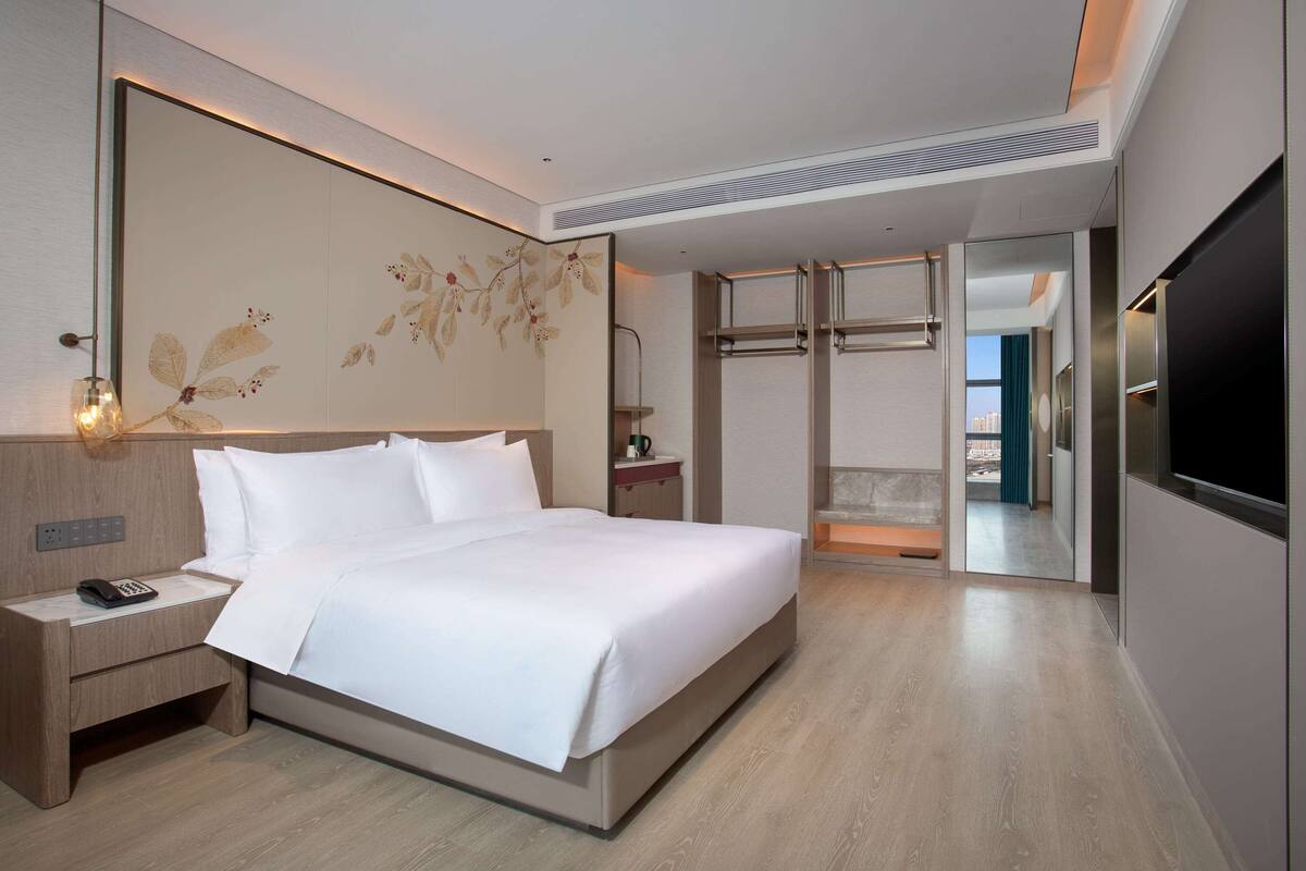 A modern hotel room with a large bed, bedside table with a phone, a mirror, and a TV.