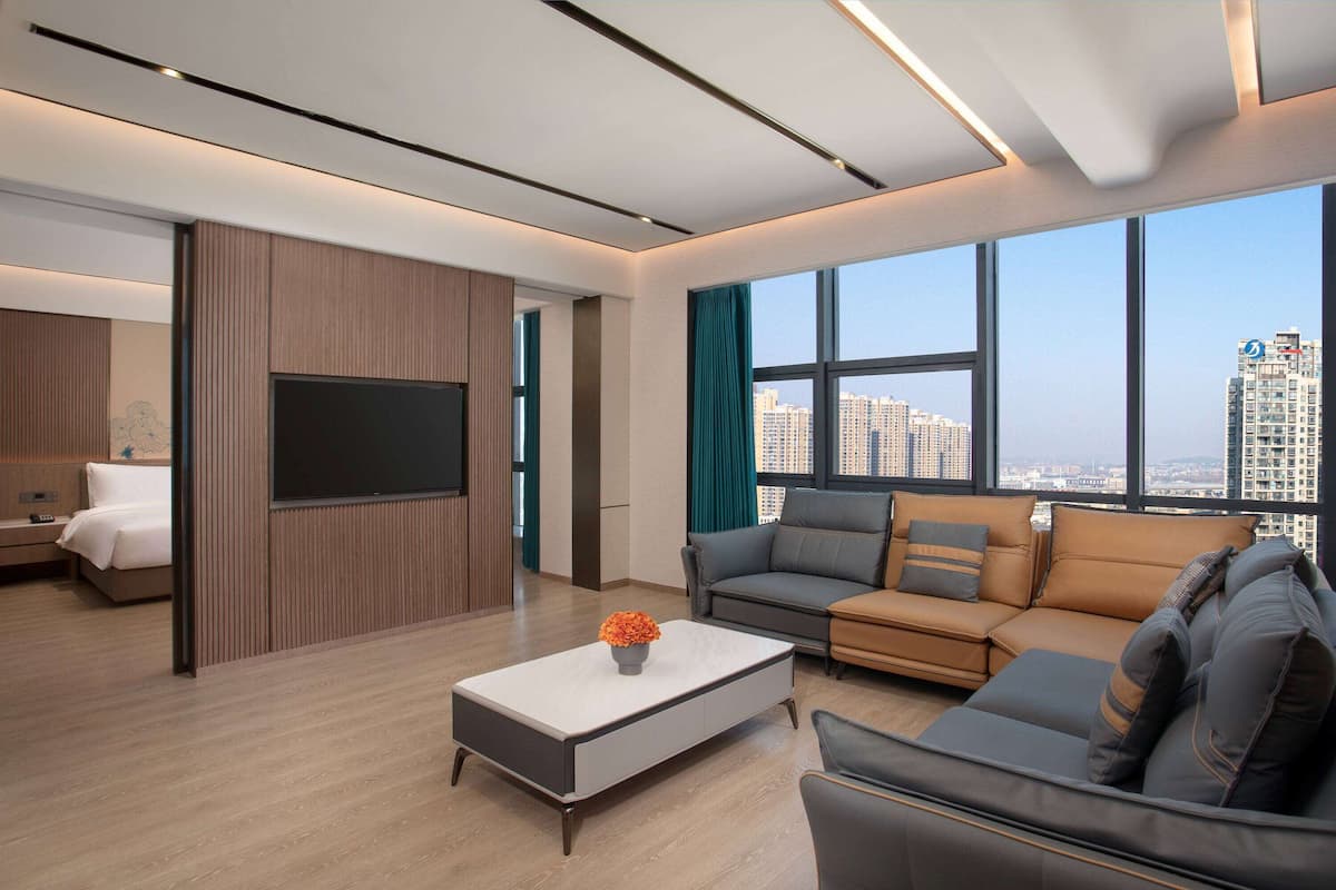 A modern living room with a flat-screen TV, a sofa, a coffee table, and a large window offering a city view.