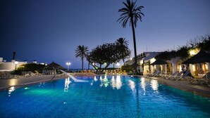 Une piscine avec des chaises longues et des palmiers, au crépuscule.