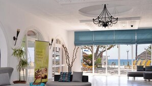 Un hall d’entrée spacieux donnant sur la plage, agrémenté d’un grand lustre et d’un espace détente aux couleurs bleu et gris.