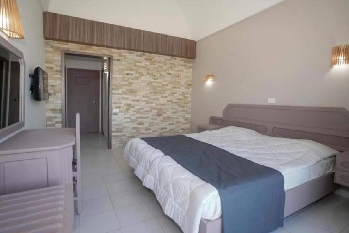 A bedroom with a bed, a dresser, a TV, and a stone wall.