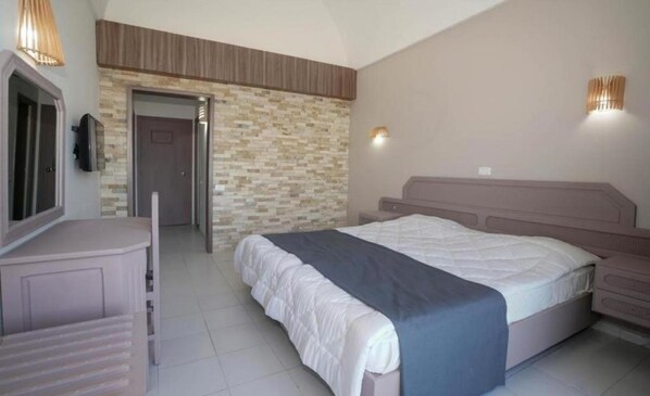 A bedroom with a bed, a dresser, a TV, and a stone wall. - Palmyra Club Nabeul (Nabeul)