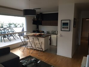 Una cocina moderna con una isla central, un comedor con sillas y vistas a través de un ventanal.