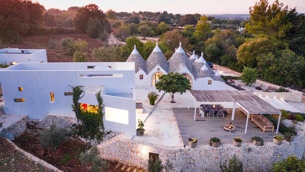 Une villa moderne avec des toits en pierre et un patio aménagé avec des sièges d’extérieur.