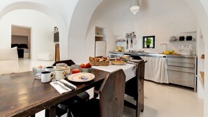 Une cuisine moderne avec des meubles blancs, un coin repas doté d’une table en bois dressée pour le petit-déjeuner, et un plafond en arc de cercle.