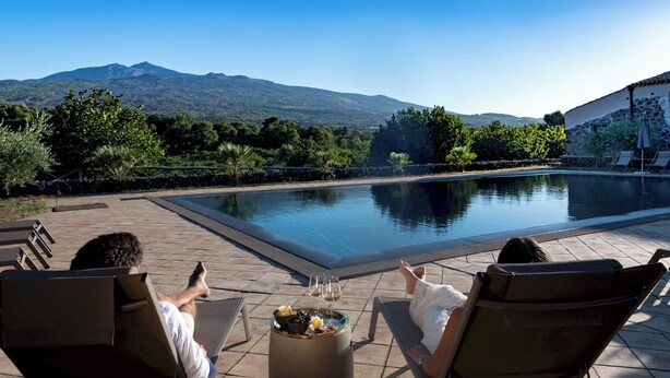 Ein Poolbereich mit Liegestühlen, einem Tisch mit Getränken und Blick auf die Berge.