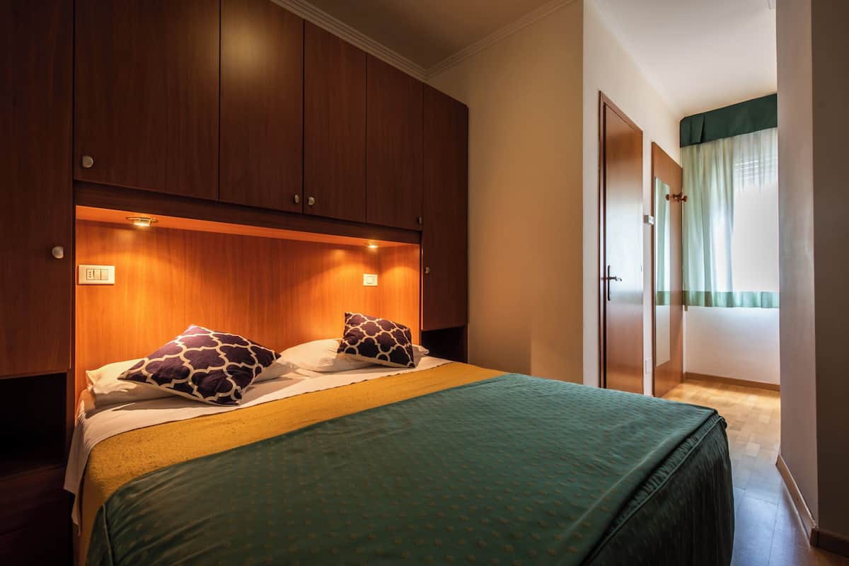 Una habitación de hotel con una cama, un armario de madera y una puerta que da a un baño.