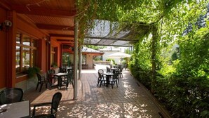 En utomhusplats med bord och stolar, omgiven av grönska och skyddad av en pergola.