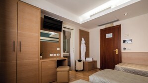 Ett hotellrum med en garderob i trä, ett skrivbord med en spegel, ett litet nattduksbord, en resväska och två sängar.