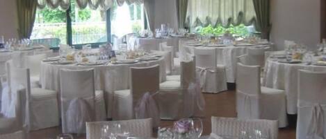 Un salón de banquetes con mesas redondas, sillas blancas y una lámpara de cristal colgante.
