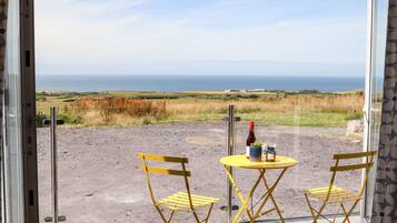 A room with a view of the sea, a table with a bottle and glasses, and two yellow chairs.