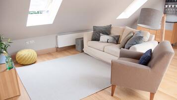 A modern loft bedroom with a high ceiling, skylights, a sofa, a chair, a lamp, and a radiator.