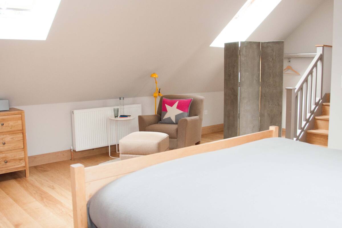 A bedroom with a sloped ceiling, a bed, a chair with a star pillow, a dresser, and a radiator.