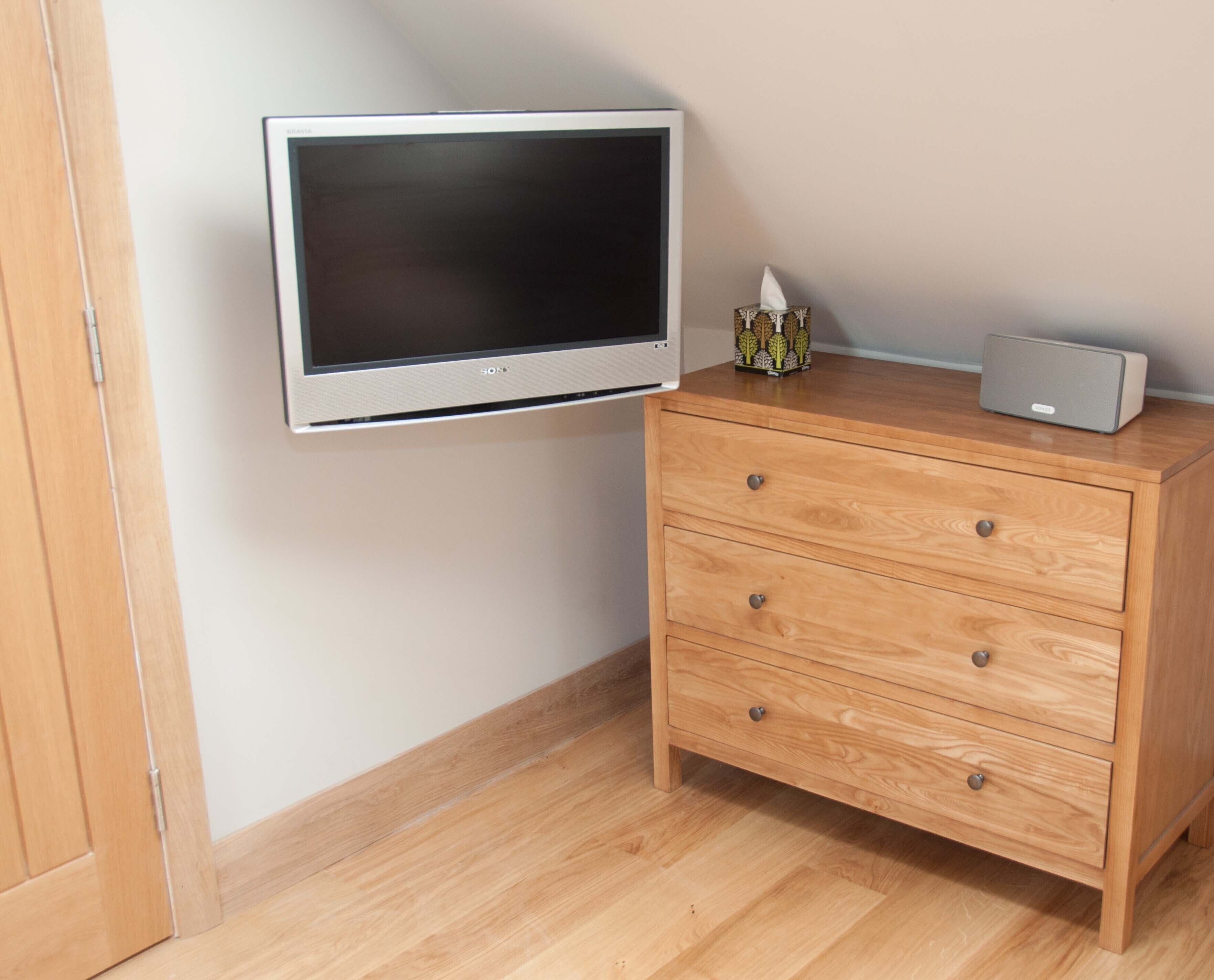 Una habitación con un aparador de madera, un televisor de pantalla plana montado en la pared y un pequeño altavoz encima del aparador.
