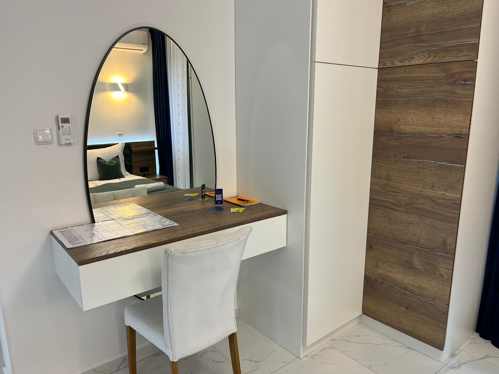 A modern bathroom with a wooden vanity, a white chair, and a large mirror.