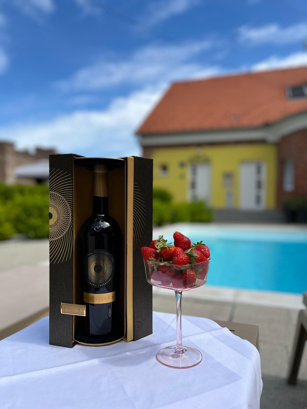 Een fles wijn in een doos met een glas aardbeien op een tafel bij een zwembad.
