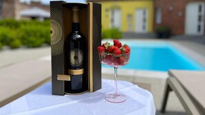 Eine Weinflasche in einer Kiste, eine Schale Erdbeeren und ein Glas auf einem Tisch am Pool.