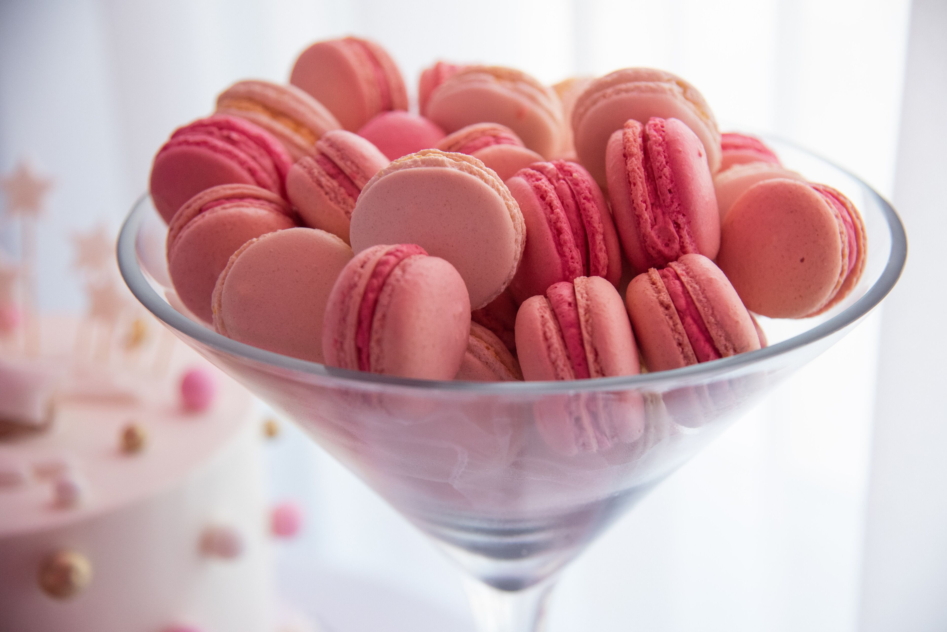 A clear glass bowl filled with pink macarons.