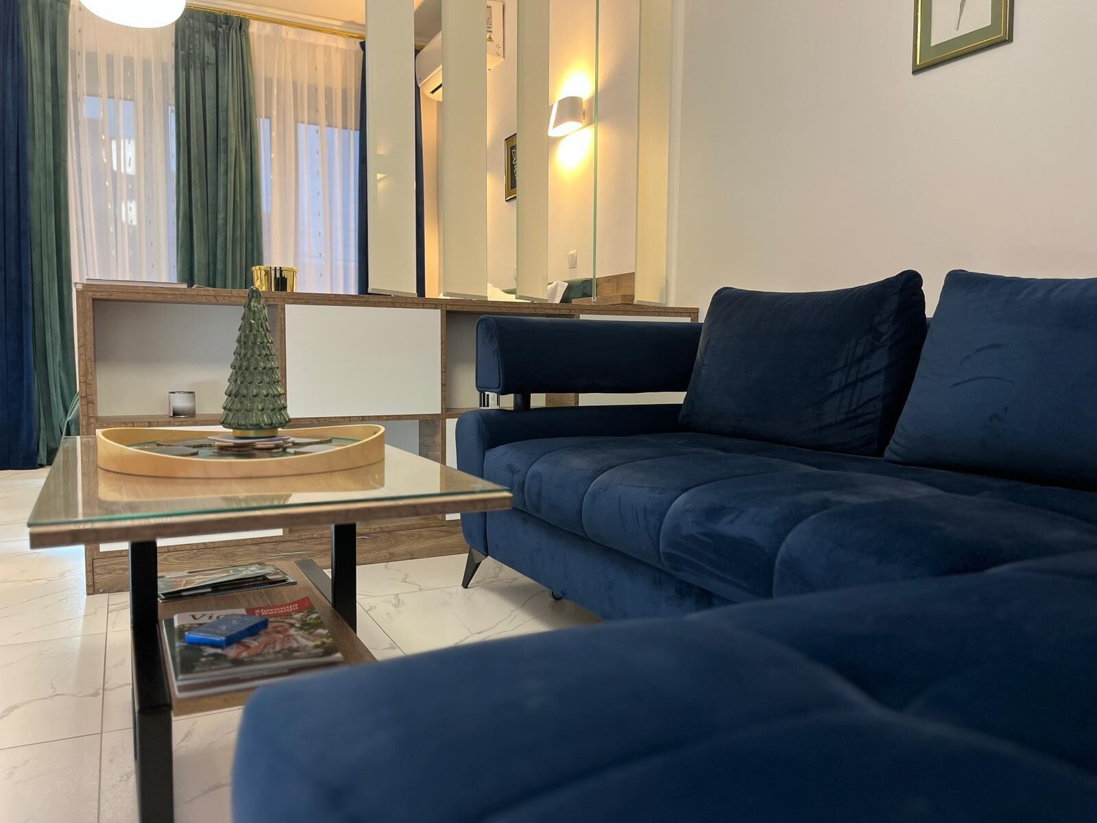 Una sala moderna con un sofá azul, una mesa de centro de cristal y un pequeño árbol de Navidad.