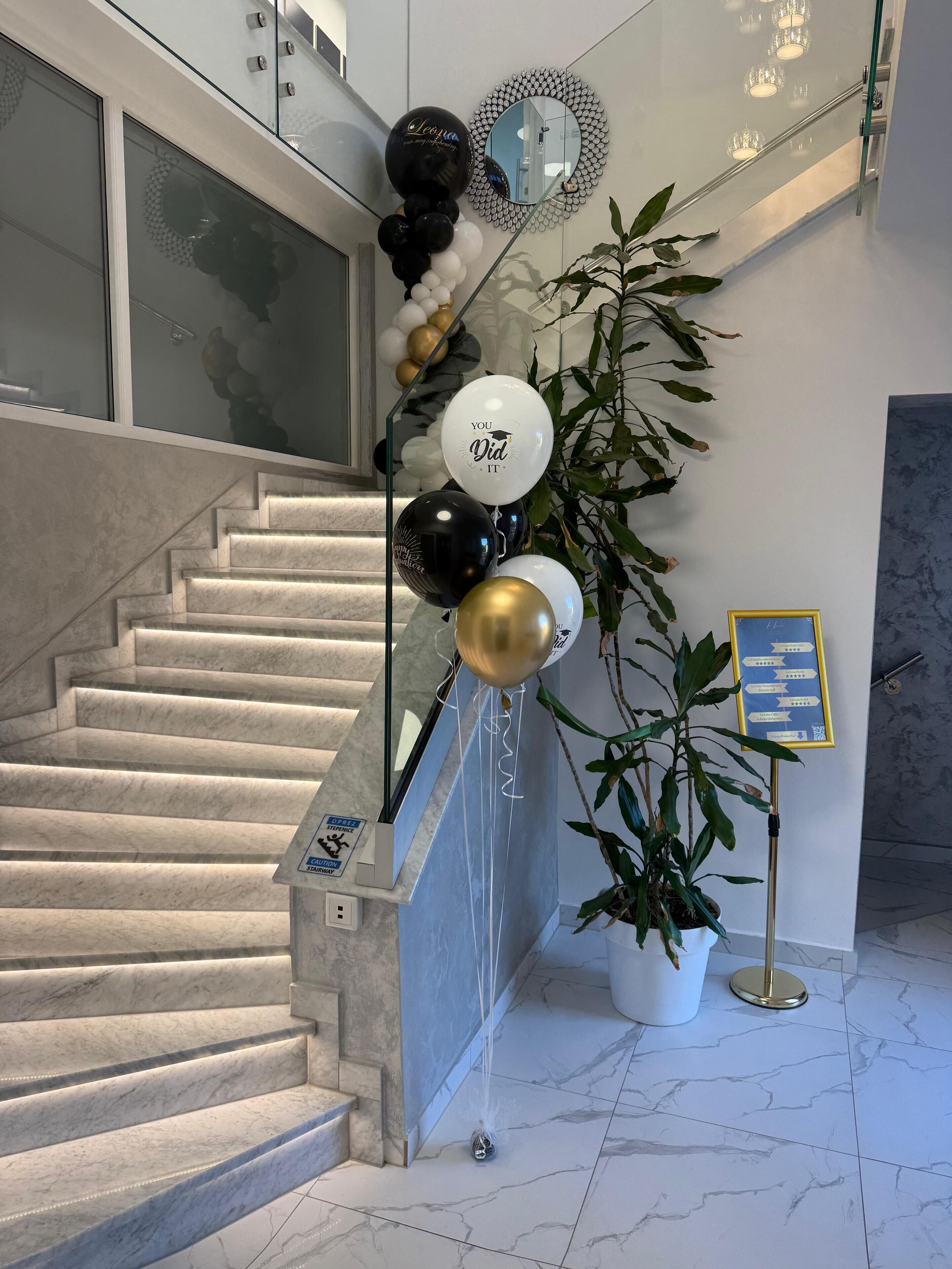 A staircase with a glass railing, a potted plant, and a sign with directional arrows.