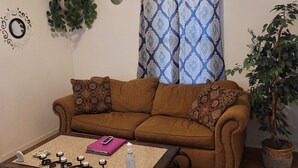 A living room with a brown sofa, a coffee table, a potted plant, and a patterned curtain. - Stylish Retreat w/ Queen Bed • Fast WiFi • Free Parking (Colorado Springs)
