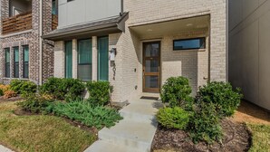 A modern townhouse with a brick facade, a front door, and a small front yard with trimmed bushes. - Contemporary Home with Office, Centrally Located (Plano)