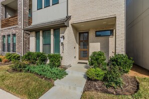 A modern townhouse with a brick facade, a front door, and a small front yard with trimmed bushes.