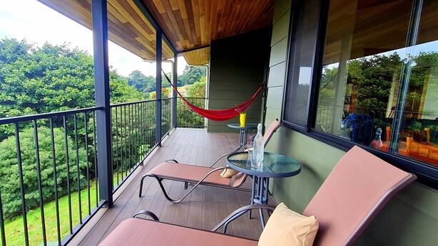 Een balkon met een hangmat, een tafel met een glas en een comfortabele stoel.